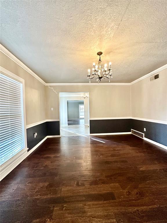 spare room featuring a textured ceiling, an inviting chandelier, crown molding, and dark hardwood / wood-style floors