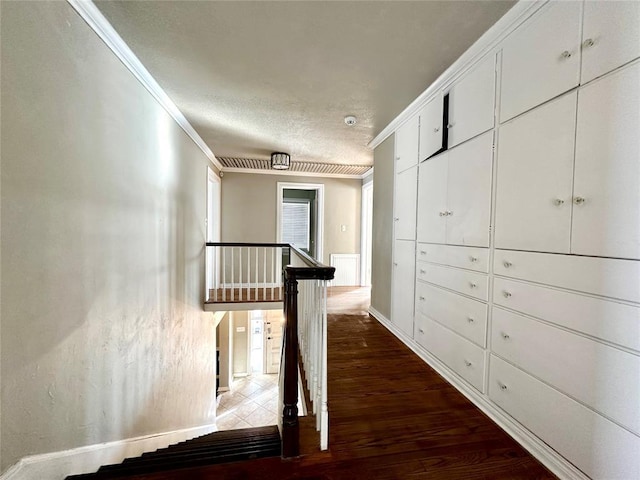 corridor with a textured ceiling, ornamental molding, and dark hardwood / wood-style floors