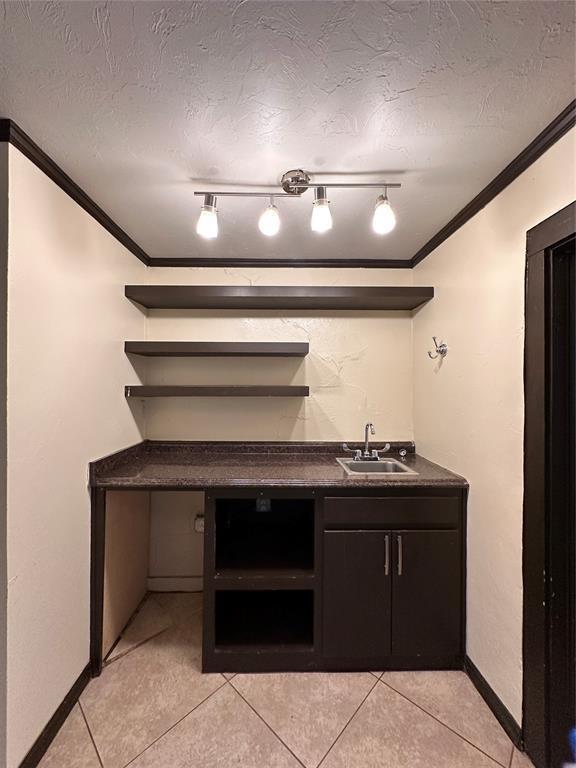 kitchen with sink, crown molding, a textured ceiling, and light tile patterned floors