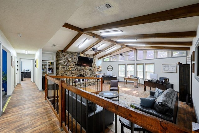 interior space featuring ceiling fan, lofted ceiling with beams, hardwood / wood-style flooring, a stone fireplace, and a textured ceiling