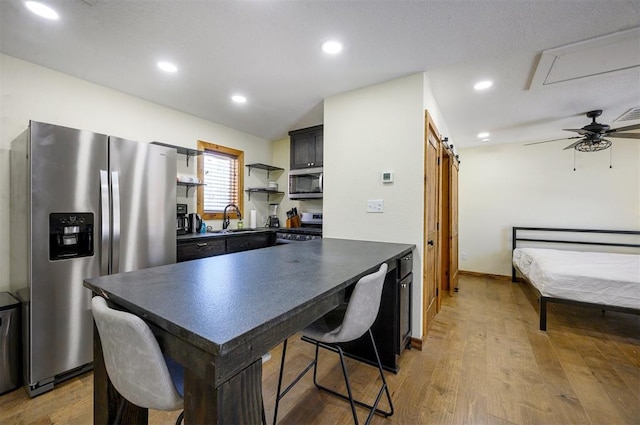 kitchen with light wood-type flooring, ceiling fan, appliances with stainless steel finishes, and a barn door