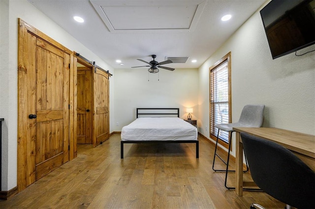 bedroom featuring ceiling fan, light hardwood / wood-style flooring, and a barn door