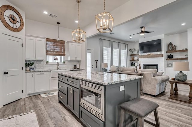 kitchen featuring white cabinetry, ceiling fan with notable chandelier, light stone countertops, stainless steel microwave, and pendant lighting