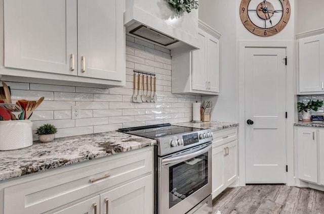 kitchen with stainless steel range with electric cooktop, white cabinets, light stone counters, light hardwood / wood-style floors, and wall chimney range hood