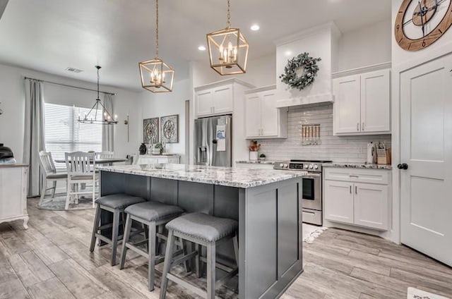 kitchen featuring stainless steel appliances, a center island, white cabinetry, decorative light fixtures, and backsplash