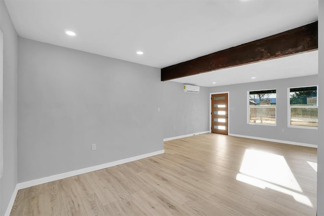 unfurnished room featuring a wall mounted AC, beam ceiling, and light hardwood / wood-style flooring