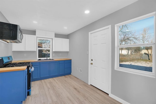 kitchen with gas range oven, white cabinetry, blue cabinetry, and wood counters