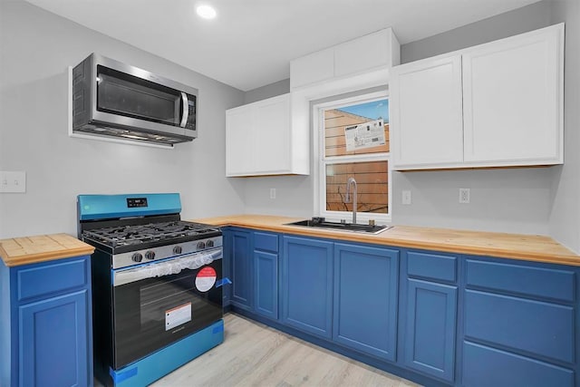 kitchen with butcher block counters, blue cabinetry, light hardwood / wood-style floors, sink, and stainless steel appliances