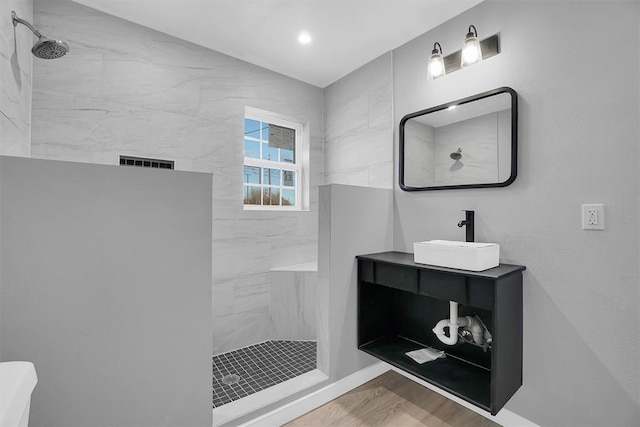 bathroom with hardwood / wood-style floors, tiled shower, and vanity