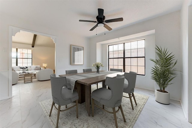 dining space featuring ceiling fan, plenty of natural light, and beamed ceiling