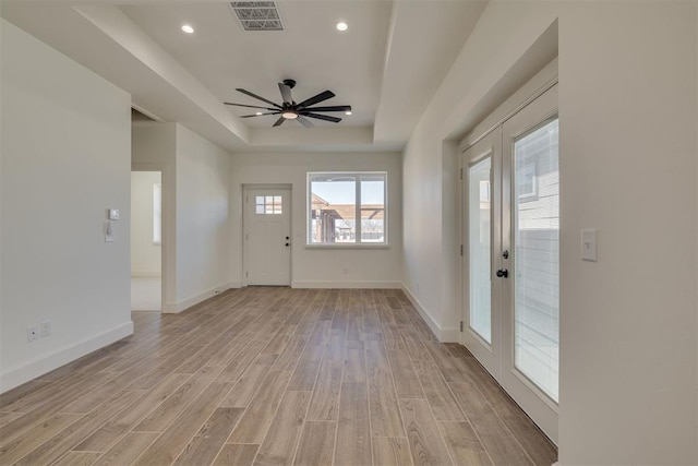 interior space with visible vents, baseboards, light wood-style flooring, a raised ceiling, and a ceiling fan