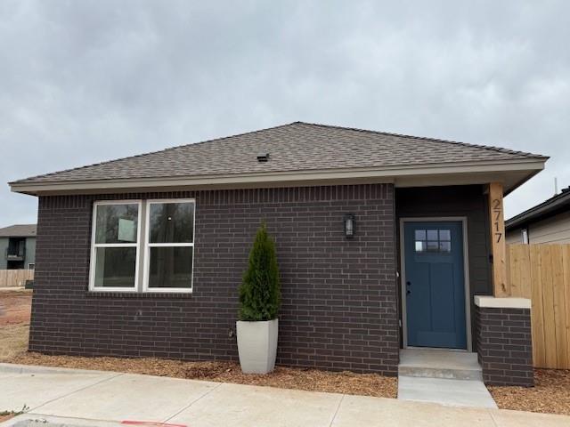 exterior space with brick siding, roof with shingles, and fence