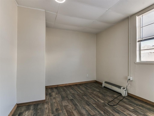 empty room with dark hardwood / wood-style flooring, baseboard heating, and a paneled ceiling