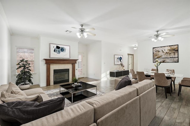 living room with ceiling fan, ornamental molding, light hardwood / wood-style floors, and a tiled fireplace