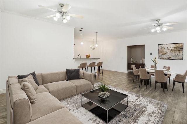 living room with ceiling fan with notable chandelier, crown molding, and light hardwood / wood-style floors