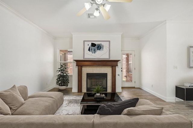 living room featuring ceiling fan, a tile fireplace, crown molding, and light hardwood / wood-style flooring