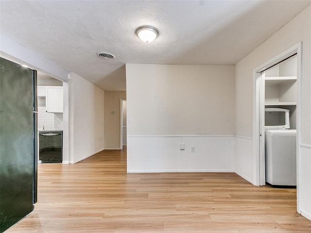 spare room featuring washer / clothes dryer, light hardwood / wood-style floors, and a textured ceiling