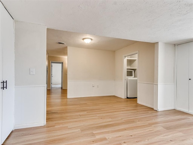 empty room featuring built in shelves, a textured ceiling, and light hardwood / wood-style floors