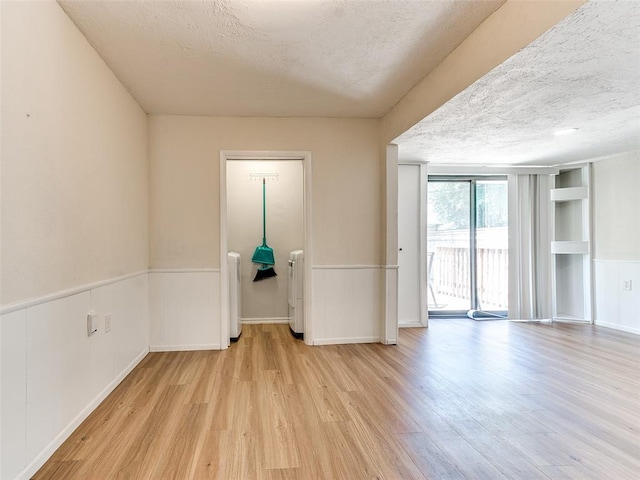 unfurnished room with a textured ceiling, light hardwood / wood-style flooring, built in features, and radiator