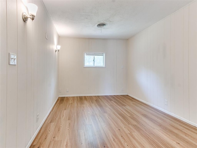 unfurnished room with light wood-type flooring and wood walls