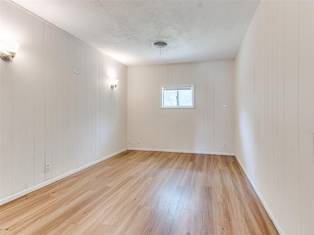 unfurnished room with wooden walls and light hardwood / wood-style flooring