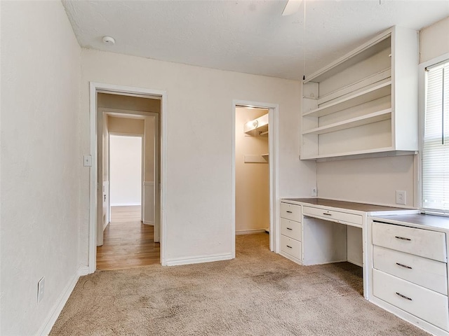 unfurnished office featuring light colored carpet, ceiling fan, and built in desk