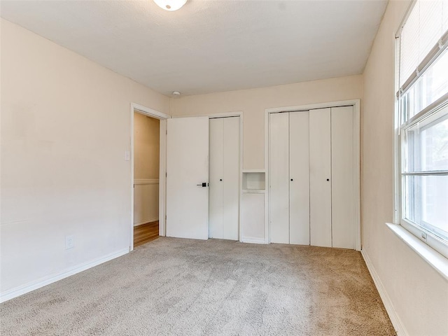 unfurnished bedroom featuring multiple closets and light colored carpet