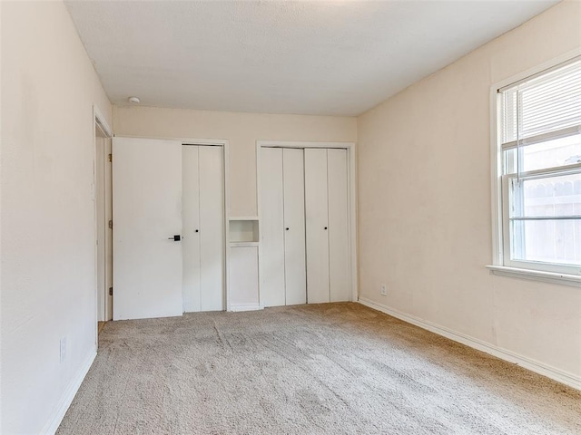 unfurnished bedroom featuring multiple windows, light carpet, and multiple closets