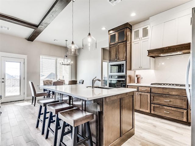 kitchen featuring oven, sink, beamed ceiling, white cabinetry, and built in microwave