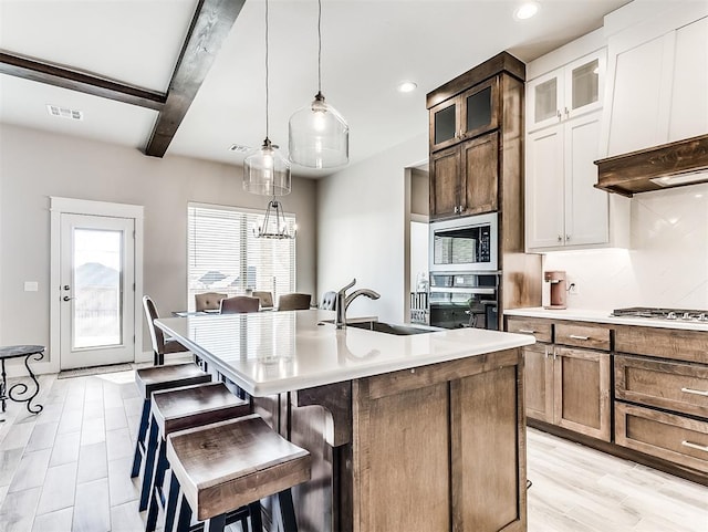 kitchen with white cabinetry, a kitchen island with sink, oven, beam ceiling, and built in microwave