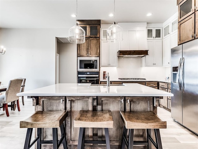 kitchen with pendant lighting, appliances with stainless steel finishes, white cabinets, an island with sink, and sink