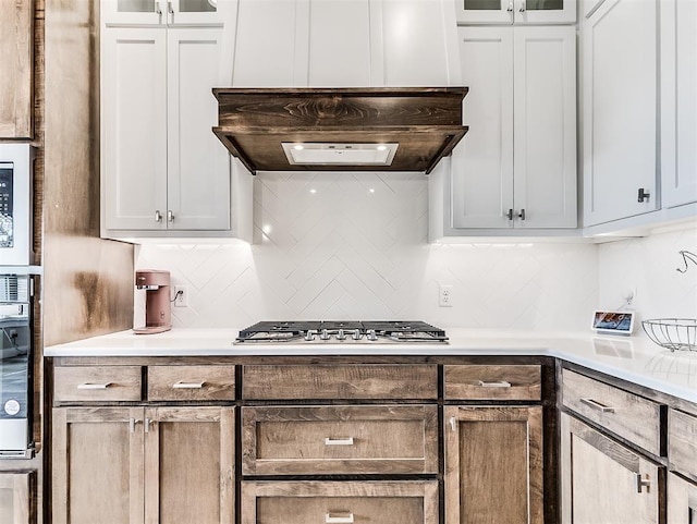 kitchen with appliances with stainless steel finishes, premium range hood, white cabinetry, and tasteful backsplash