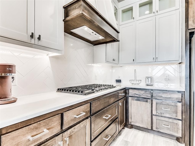 kitchen featuring decorative backsplash, white cabinetry, stainless steel gas stovetop, and custom exhaust hood