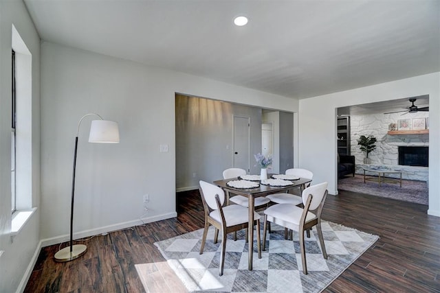 dining space featuring dark hardwood / wood-style flooring, ceiling fan, built in features, and a stone fireplace