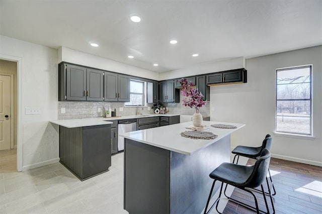 kitchen featuring kitchen peninsula, stainless steel dishwasher, tasteful backsplash, a breakfast bar area, and sink