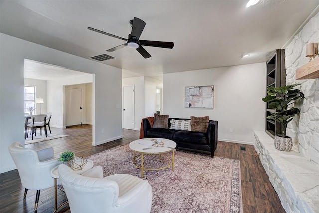 living room with dark hardwood / wood-style flooring, ceiling fan, and a stone fireplace