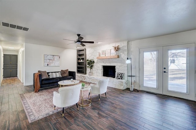 living room with ceiling fan, built in features, french doors, and a stone fireplace