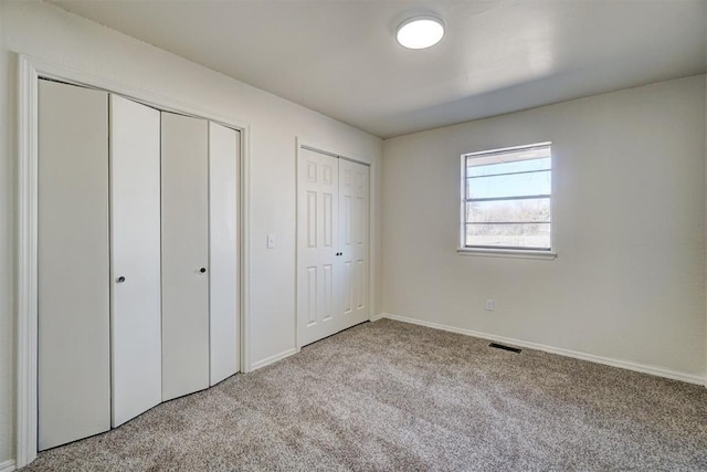 unfurnished bedroom featuring two closets and light colored carpet