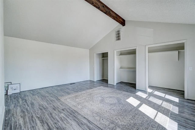 unfurnished bedroom featuring a textured ceiling, beamed ceiling, two closets, dark hardwood / wood-style floors, and high vaulted ceiling