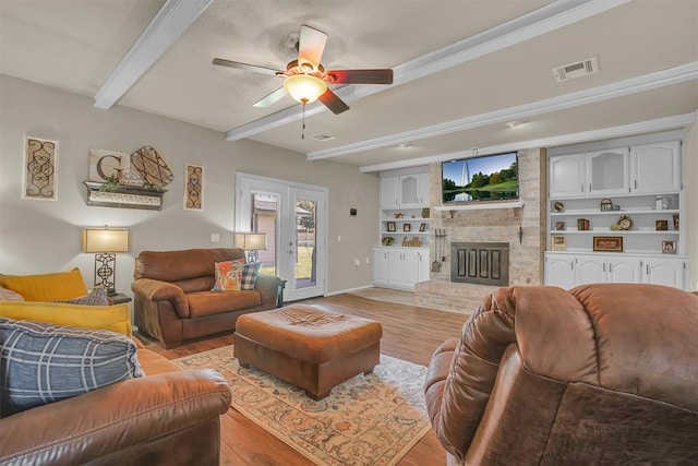 living room featuring a large fireplace, built in shelves, light wood-type flooring, ceiling fan, and beamed ceiling