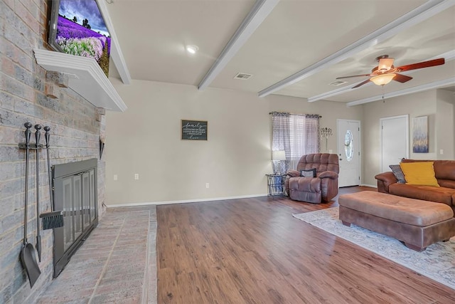 living room featuring hardwood / wood-style flooring, ceiling fan, beamed ceiling, and a brick fireplace