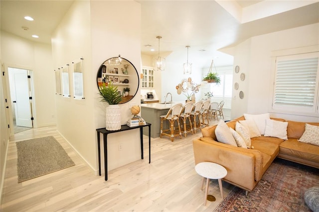 living room featuring sink, a high ceiling, a chandelier, and light wood-type flooring