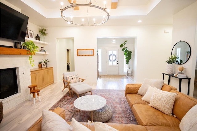 living room with an inviting chandelier, a tray ceiling, a brick fireplace, and light hardwood / wood-style flooring