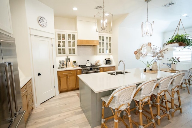 kitchen with pendant lighting, sink, high quality appliances, custom range hood, and an island with sink