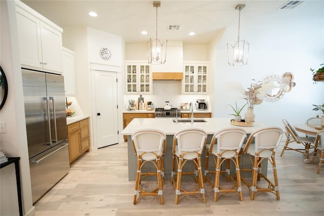 kitchen featuring appliances with stainless steel finishes, sink, white cabinets, a kitchen island with sink, and custom range hood