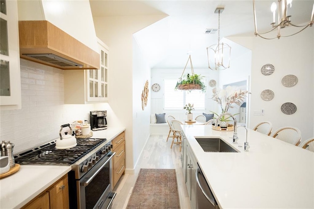 kitchen with decorative light fixtures, tasteful backsplash, sink, stainless steel appliances, and custom range hood