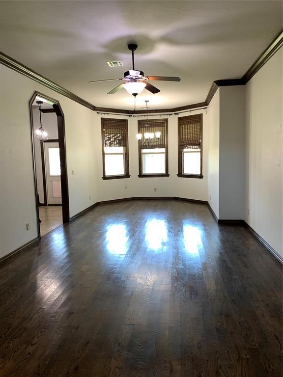 empty room featuring ceiling fan with notable chandelier, ornamental molding, and dark wood-type flooring