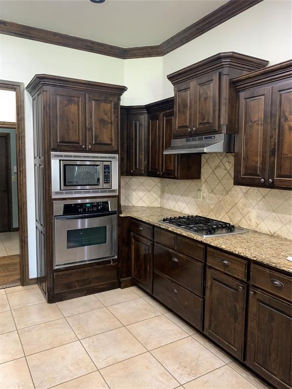 kitchen with stainless steel appliances, dark brown cabinetry, light tile patterned floors, and light stone countertops