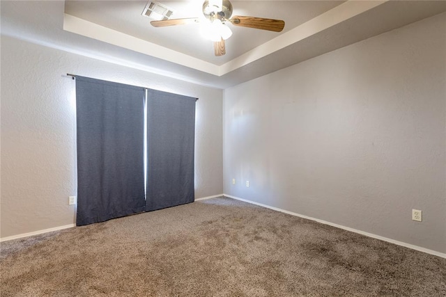 unfurnished room featuring a raised ceiling, carpet, and ceiling fan