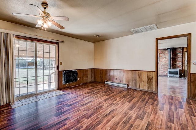 spare room featuring ceiling fan, a wood stove, dark wood-type flooring, baseboard heating, and heating unit